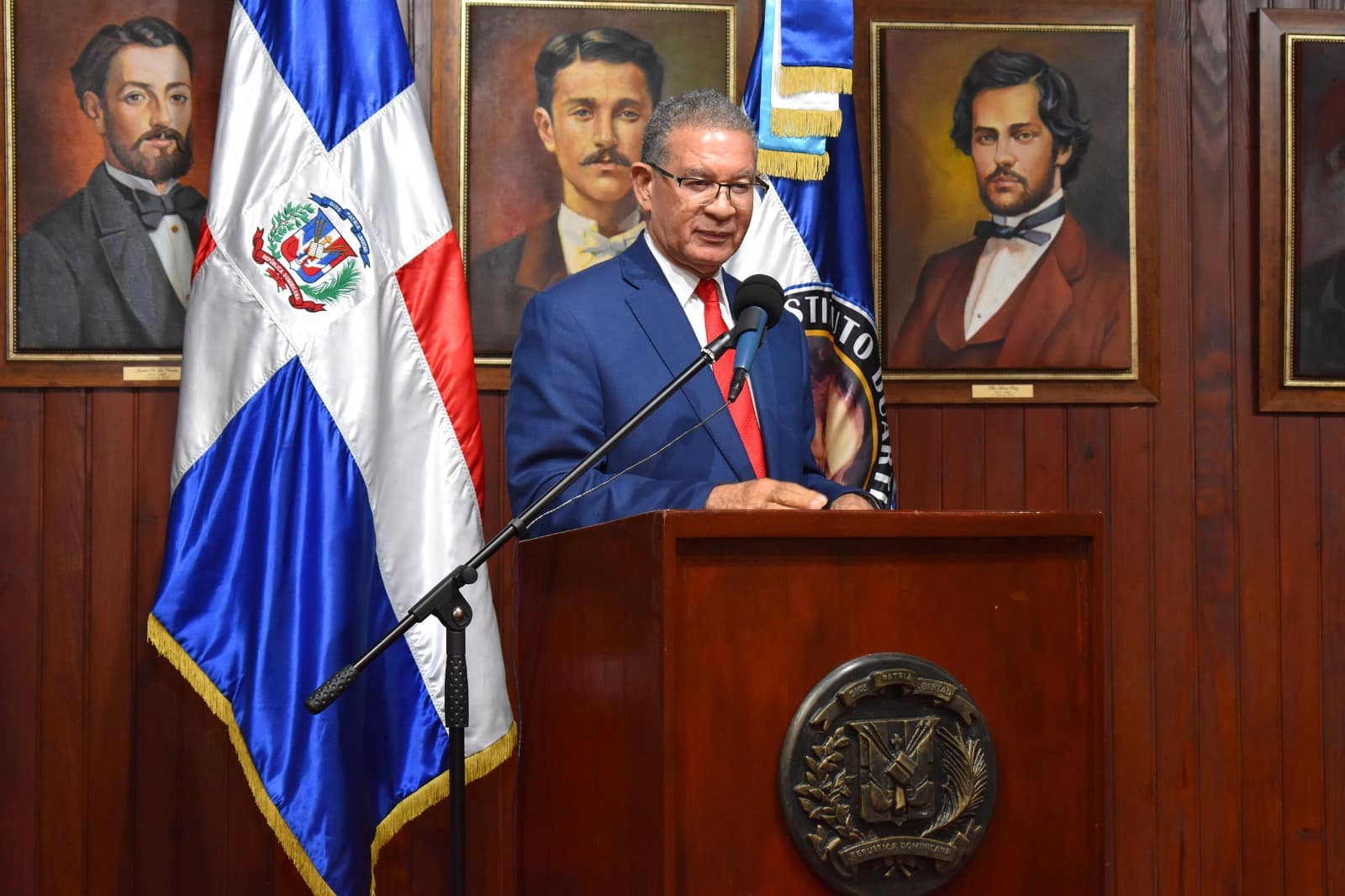 Wilson Gómez Ramírez durante su intervención en el podio del Instituto Duartiano, con la bandera dominicana al fondo.